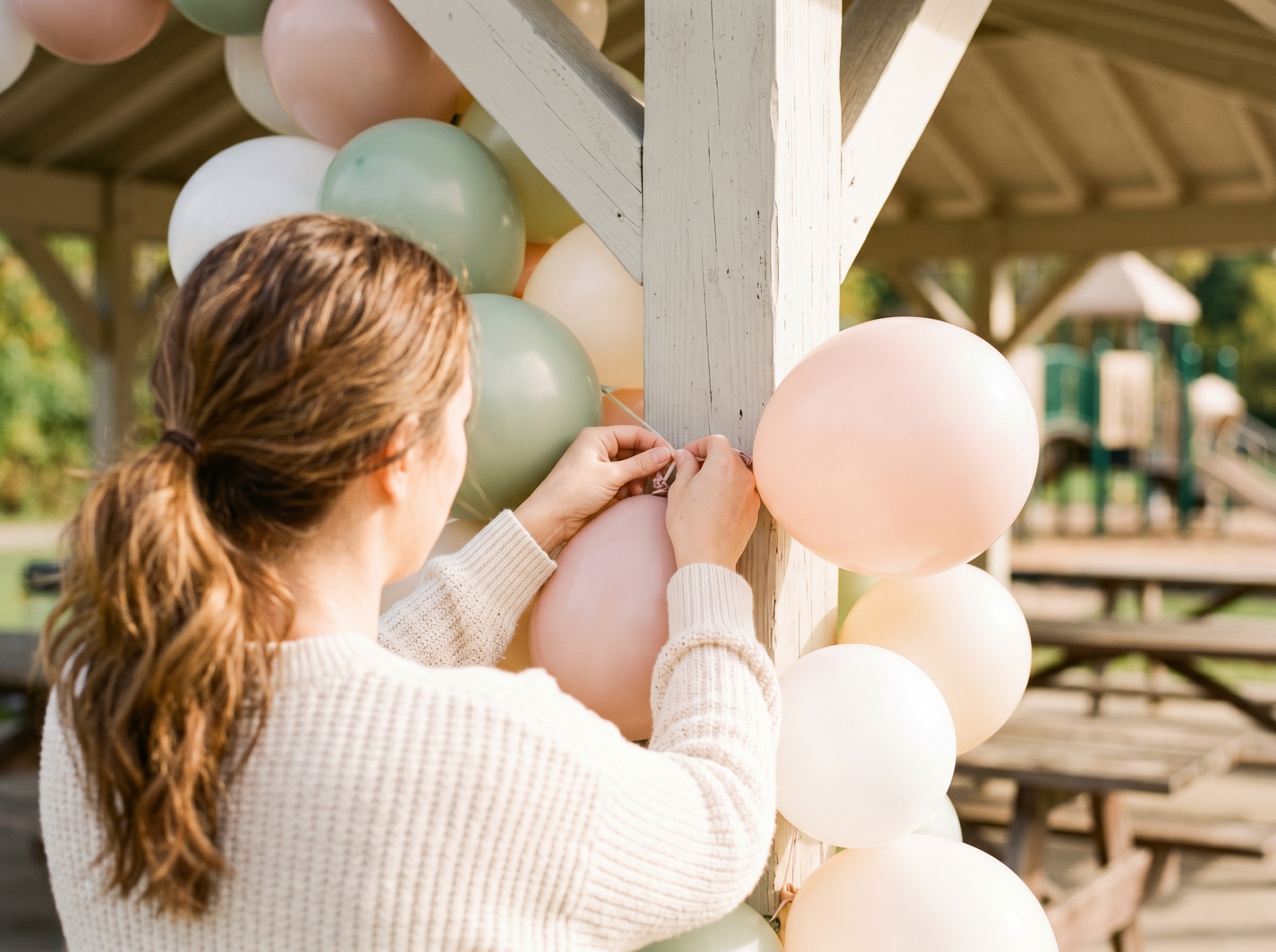Hands tying colorful balloons to wooden picnic shelter beam for birthday party decor