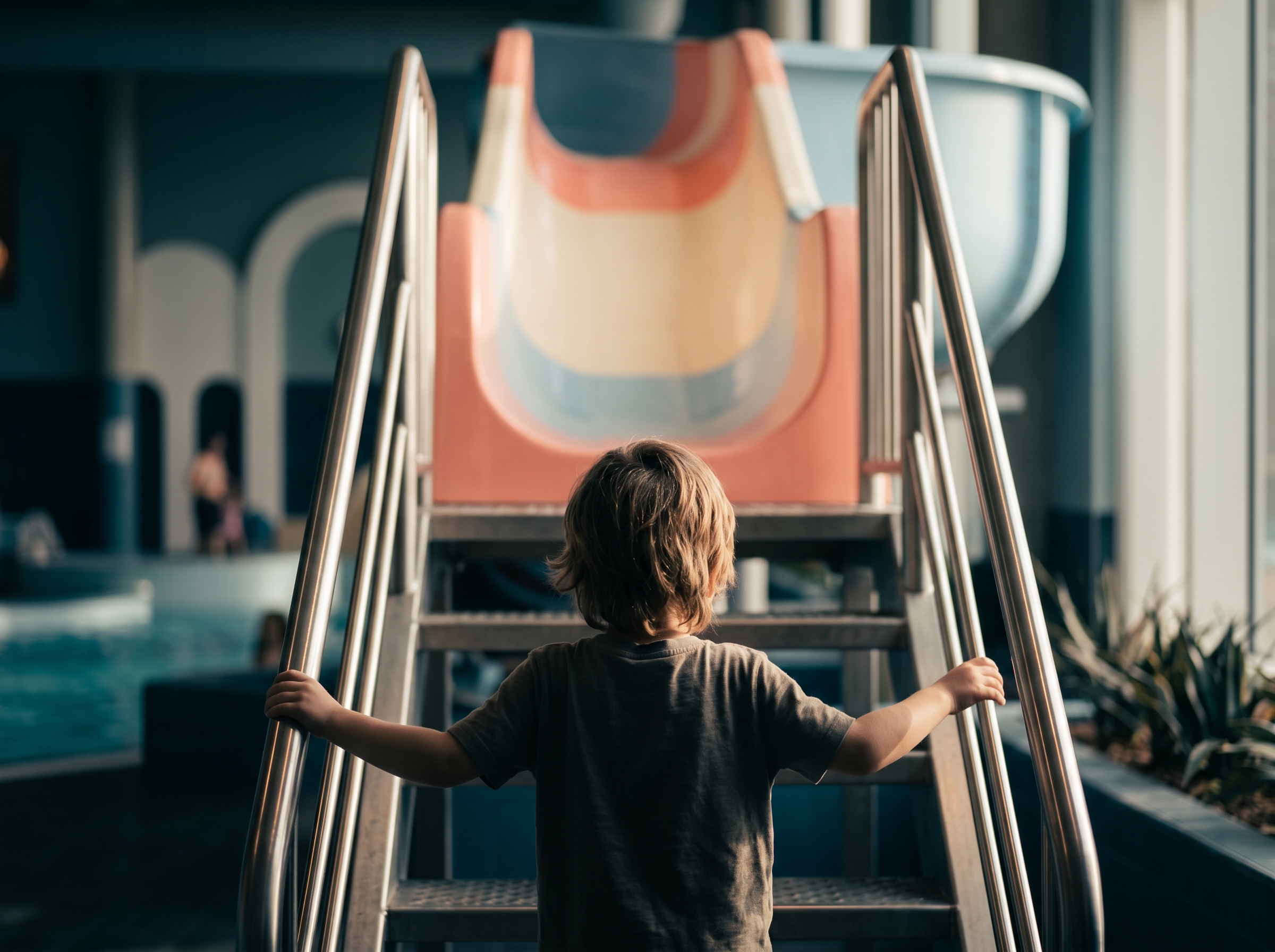 Child climbing the steps of a colorful slide, photographed from behind with natural light